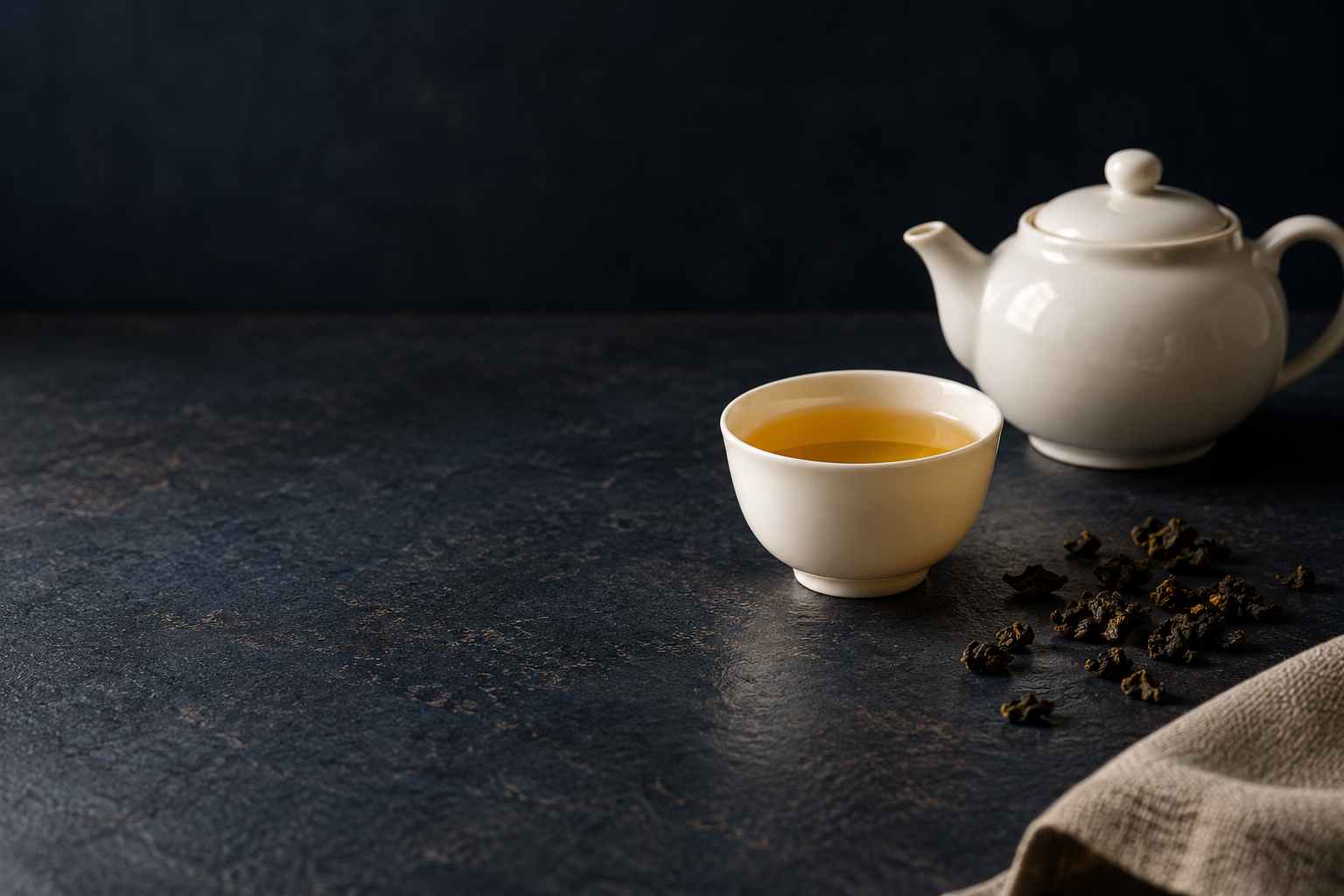 藏青石桌上的白瓷茶壺與金黃茶湯，日常飲茶意象